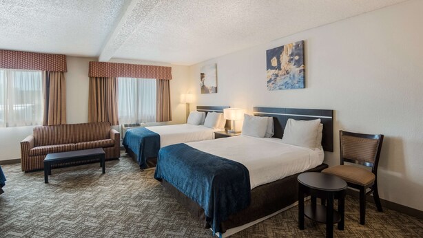 A hotel room with two beds, a sofa, a chair, a small table, and a painting on the wall.
