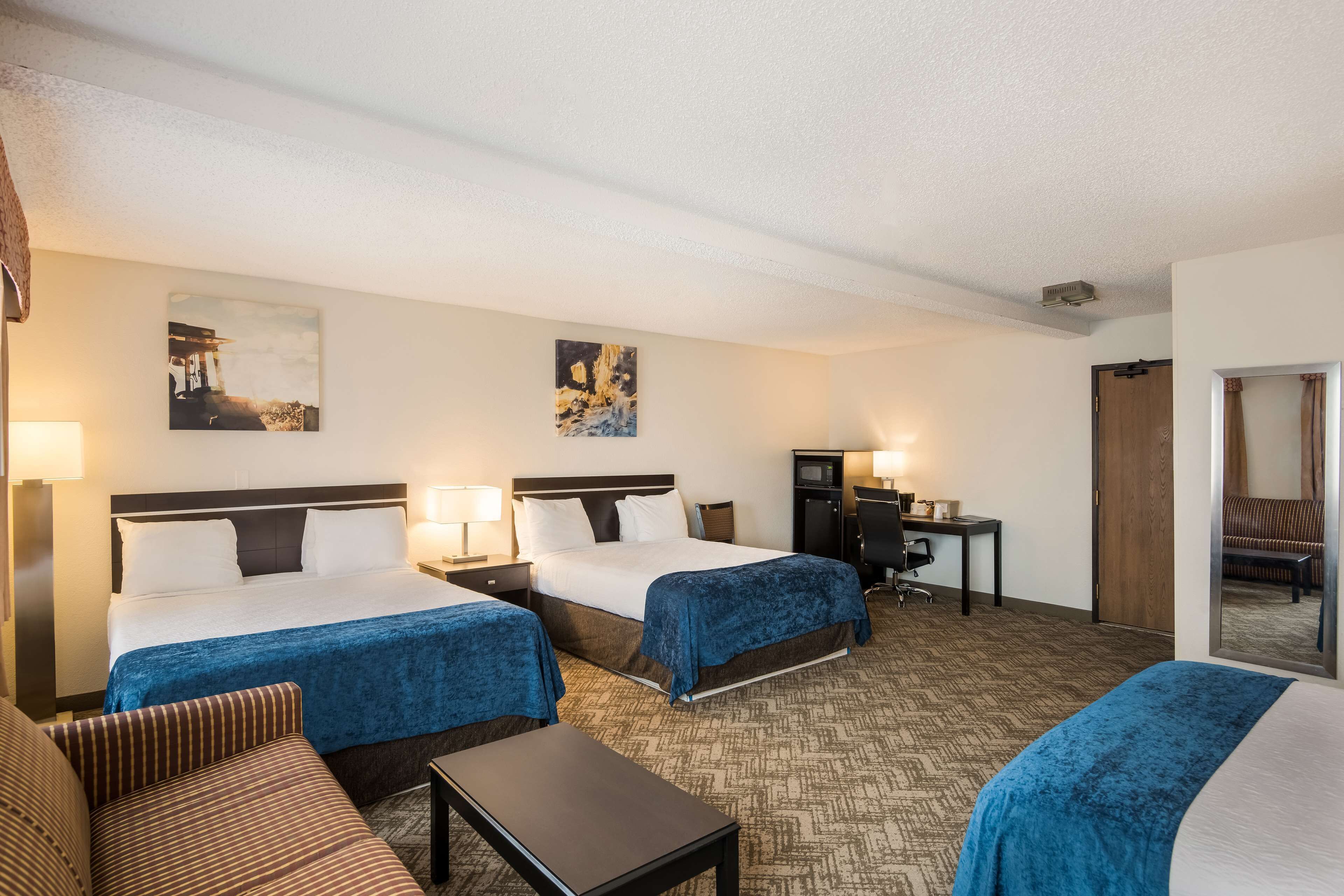 A hotel room with two beds, a desk, a chair, and a sofa.