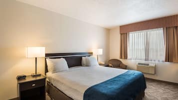 Une chambre d’hôtel avec un grand lit, deux tables de chevet avec des lampes, une chaise, une fenêtre avec des rideaux et un appareil de climatisation.