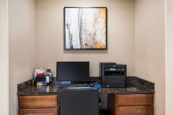 A hotel workspace with a desktop computer, printer, and a large abstract painting on the wall.
