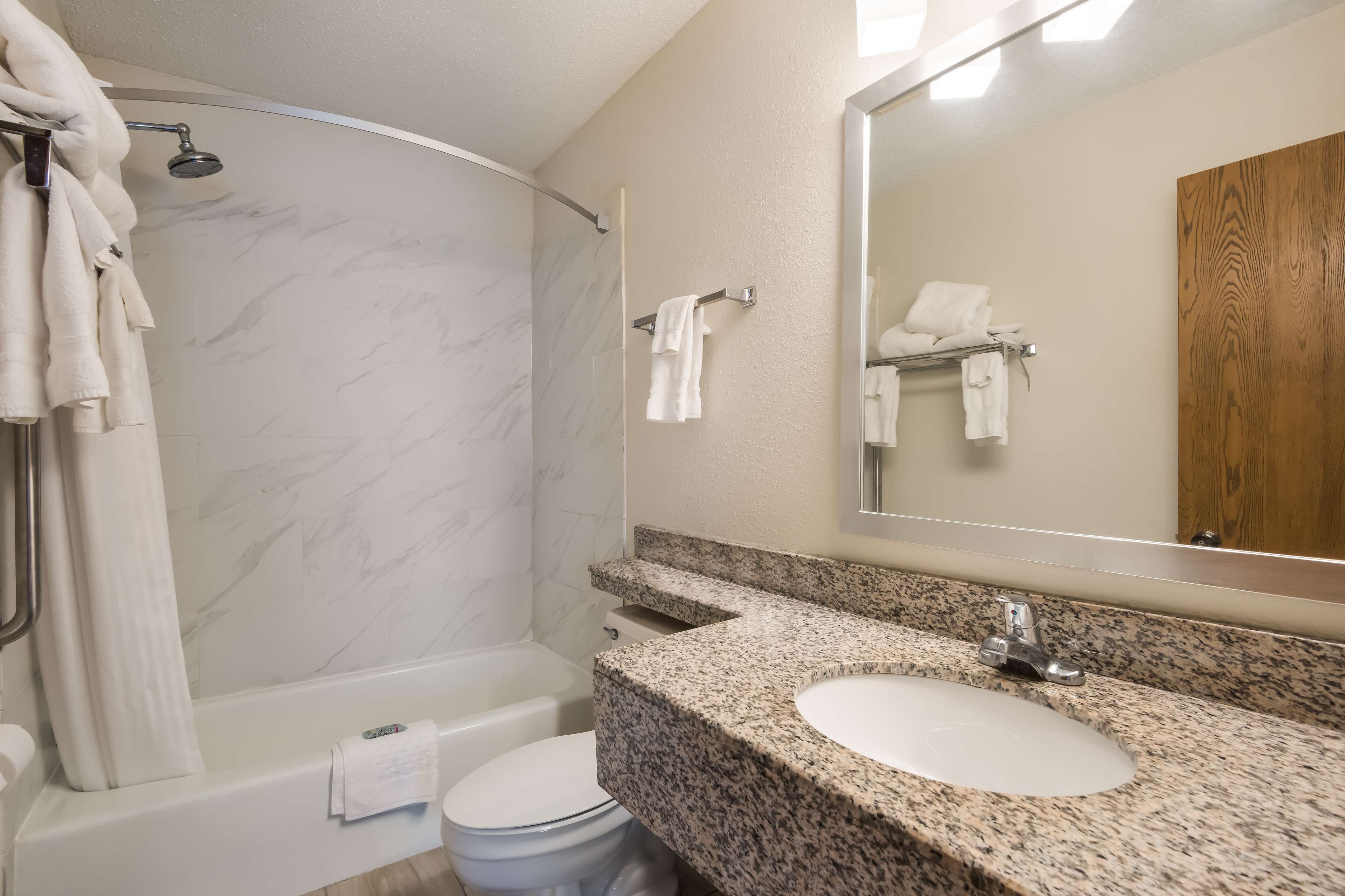 Un baño con ducha de mármol, bañera, inodoro y lavamanos sobre encimera de granito.