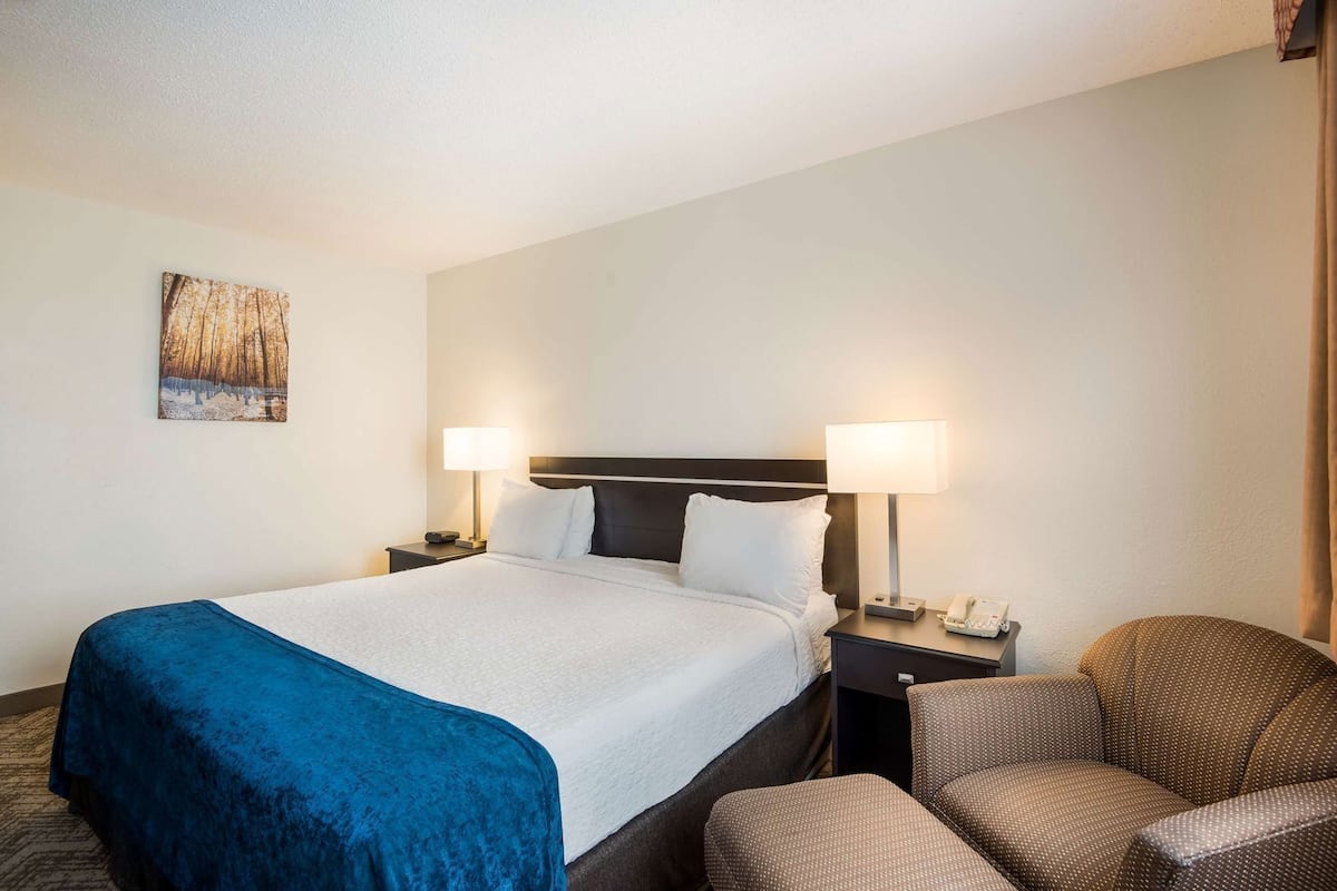 A hotel room with a bed, two bedside tables, a chair, and a painting on the wall.