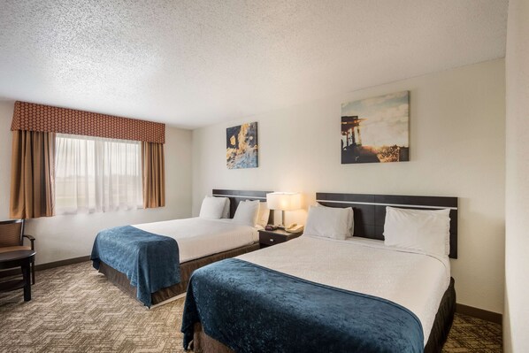 A hotel room with two beds, a desk, and a chair. There are two paintings on the walls.