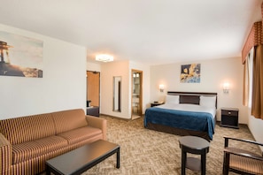 A hotel room with a bed, a sofa, a small table, a chair, a nightstand, and a painting on the wall.