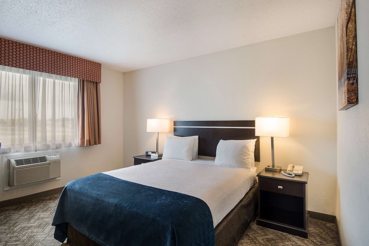 A hotel room with a large bed, two bedside lamps, a nightstand with a phone, and a window with curtains.