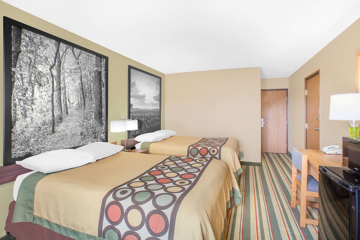 A hotel room with two beds, a desk, a chair, a TV, and a door.