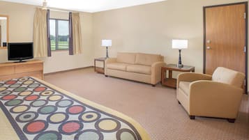 Een hotelkamer met een bank, fauteuil, televisie, lampen en een tapijt met een rond patroon.