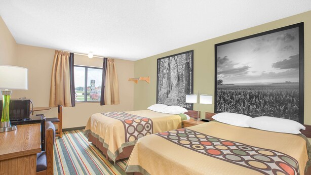 Habitación de hotel con dos camas, un escritorio, una silla y un ventanal grande.
