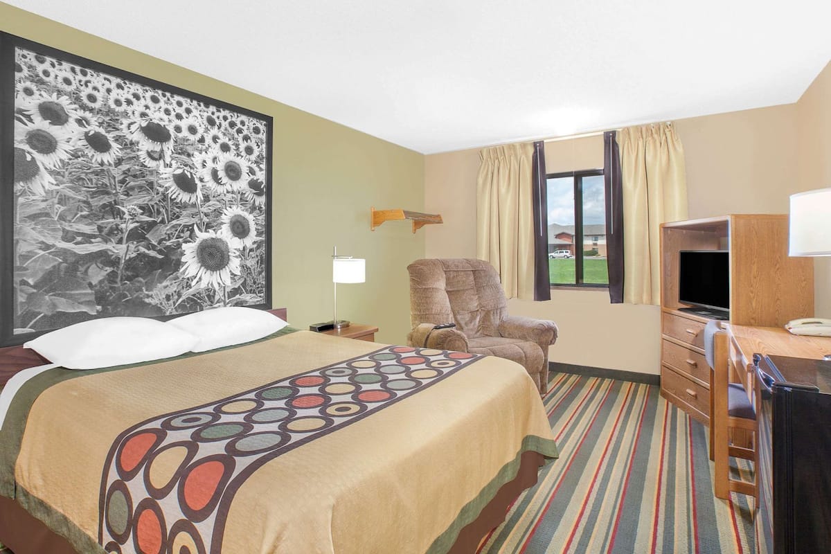 A hotel room with a bed, a chair, a desk with a TV, and a large window.