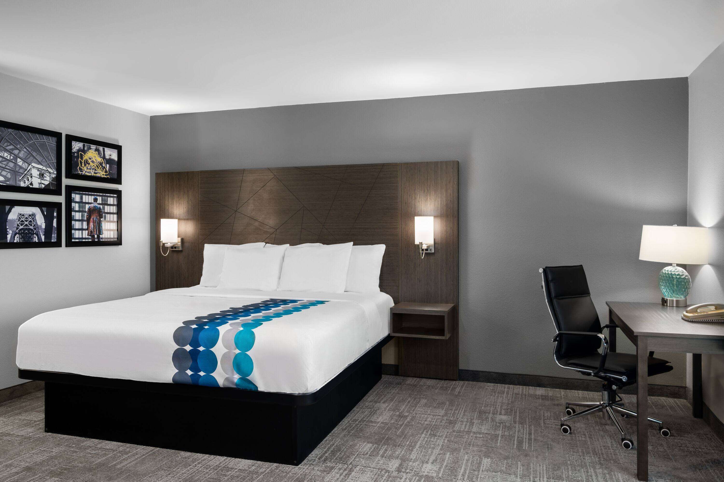 A hotel room with a large bed, two bedside lamps, a desk with a chair, and framed pictures on the wall.