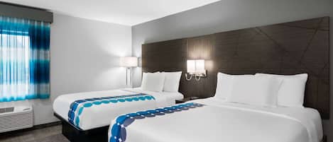 Camera d'albergo con due letti, ognuno con copripiumino bianco e dettagli blu, un'ampia finestra con tende azzurre e un lampadario fissato alla parete.