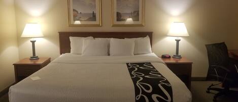 Una habitación de hotel con una cama grande, dos lámparas de noche, un reloj y dos cuadros en la pared.