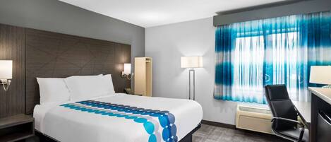 Habitación de hotel con una cama grande, un escritorio, una silla y una ventana con cortinas.