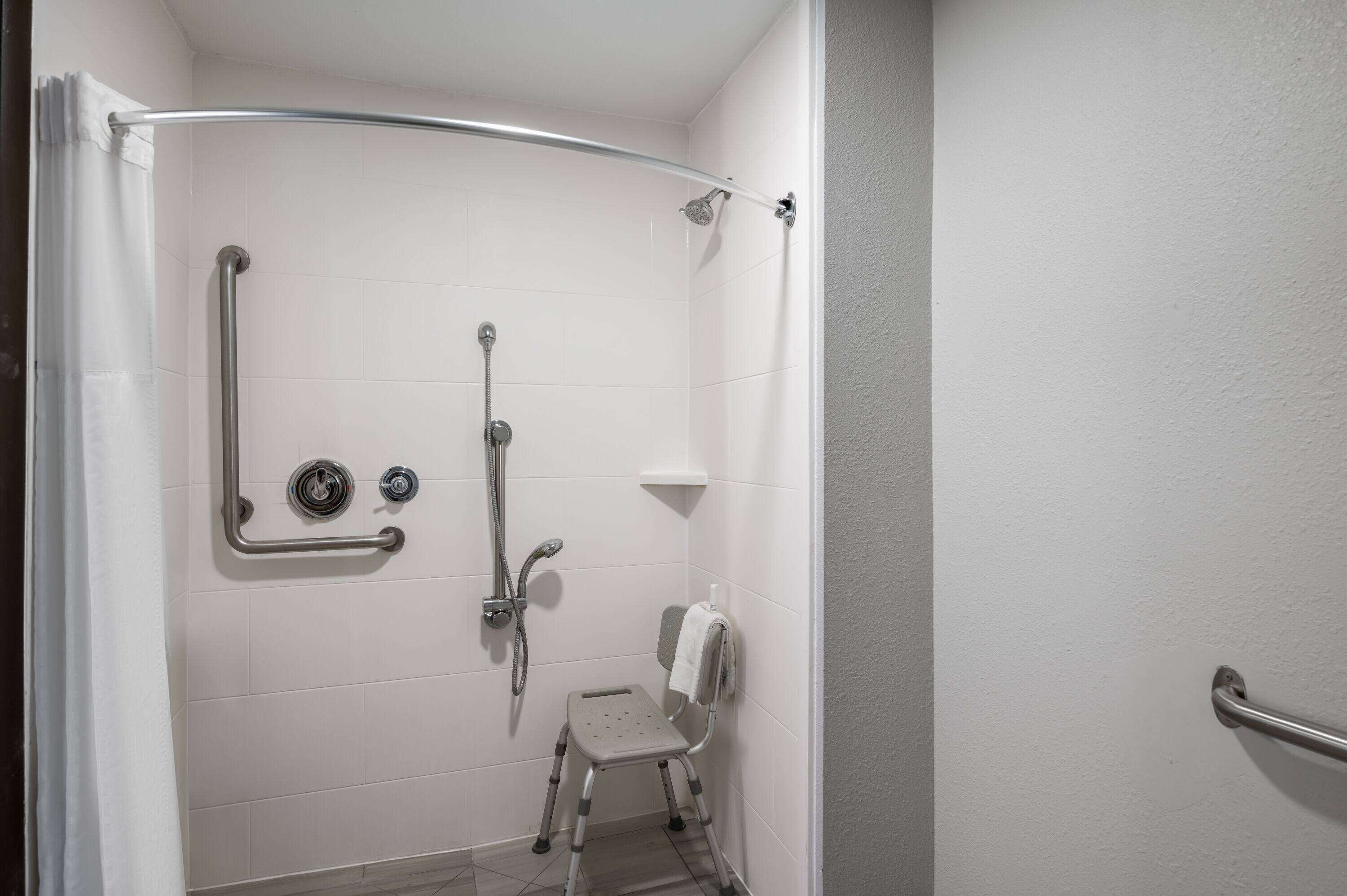 Un espace douche équipé d’une barre d’appui, d’un siège de douche et d’un pommeau de douche à main.