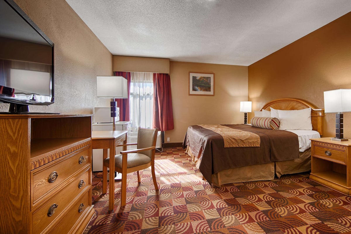 Une chambre d’hôtel comprenant un lit, un bureau, une chaise, une commode et un téléviseur.