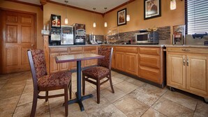 A kitchen with wooden cabinets, a dining table, two patterned chairs, a microwave, and a coffee machine. - Best Western Martinsville Inn (Martinsville)