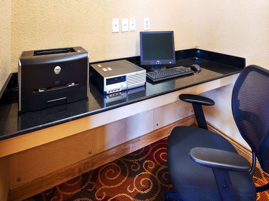 Un espacio de trabajo compacto con una computadora de escritorio, una impresora y un teclado sobre un escritorio negro.