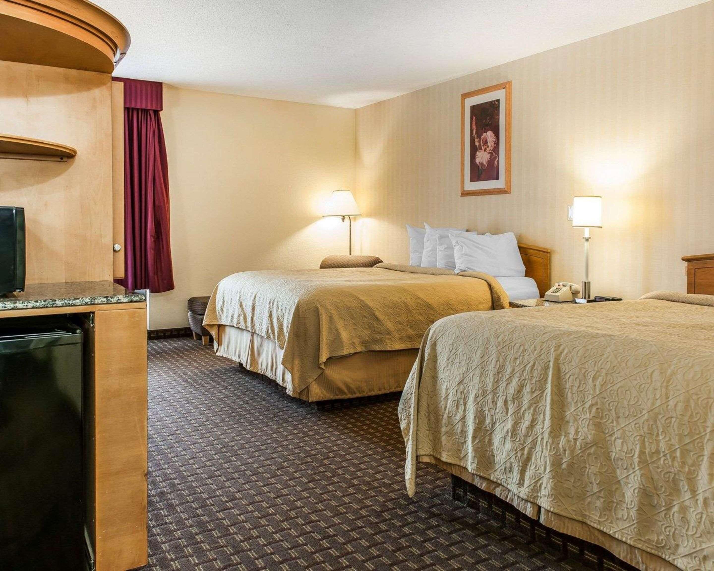 A hotel room with two beds, a desk with a television, and a bathroom.