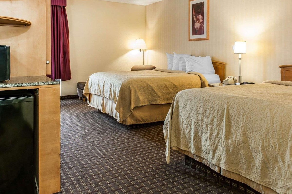 A hotel room with two beds, a desk with a television, and a bathroom.