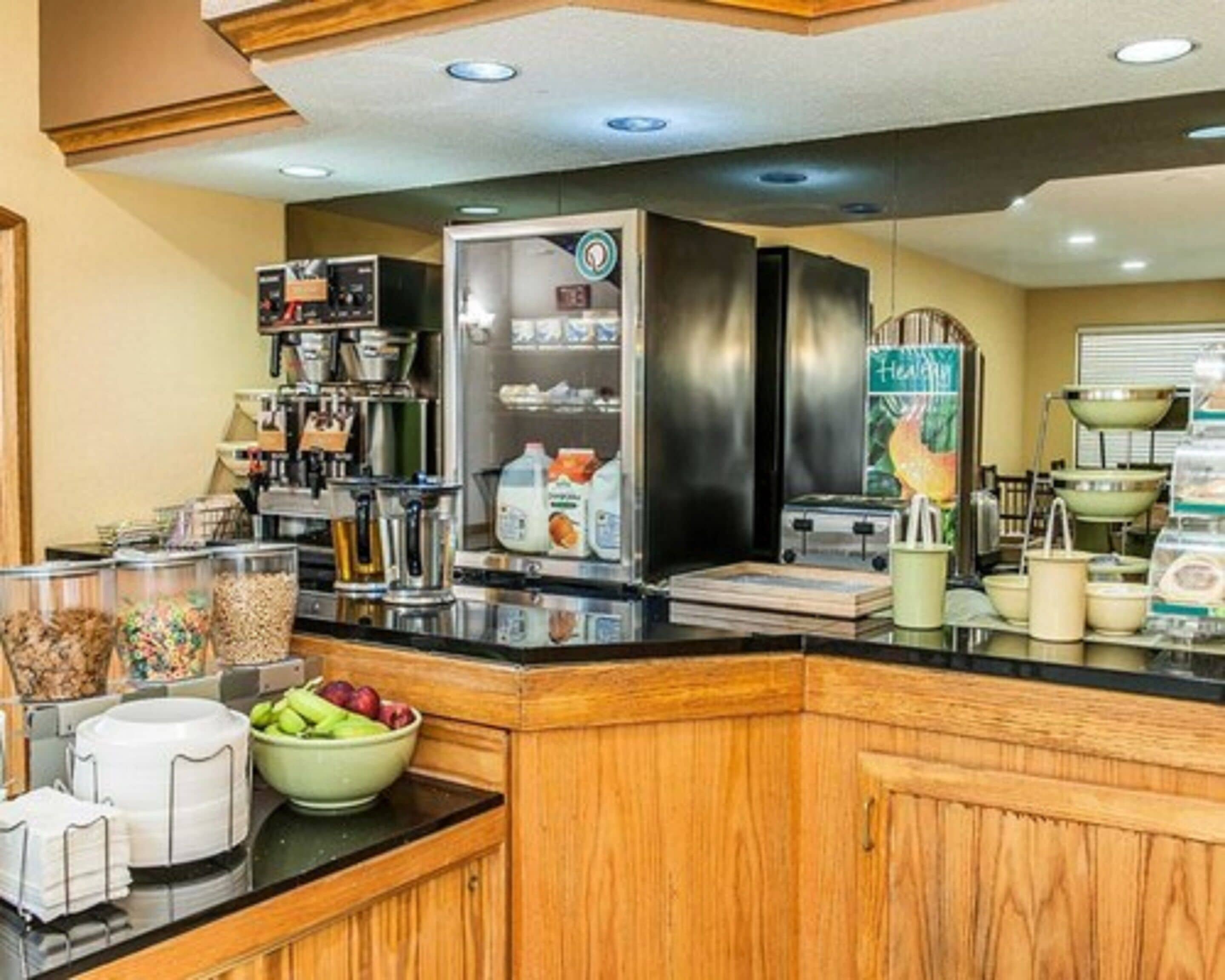 A breakfast bar with a coffee machine, a refrigerator stocked with beverages, and various food items.