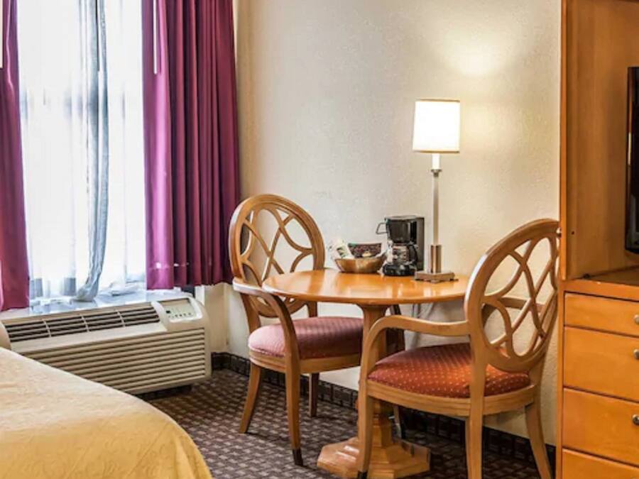 Habitación de hotel con cama, escritorio, silla, lámpara y armario.