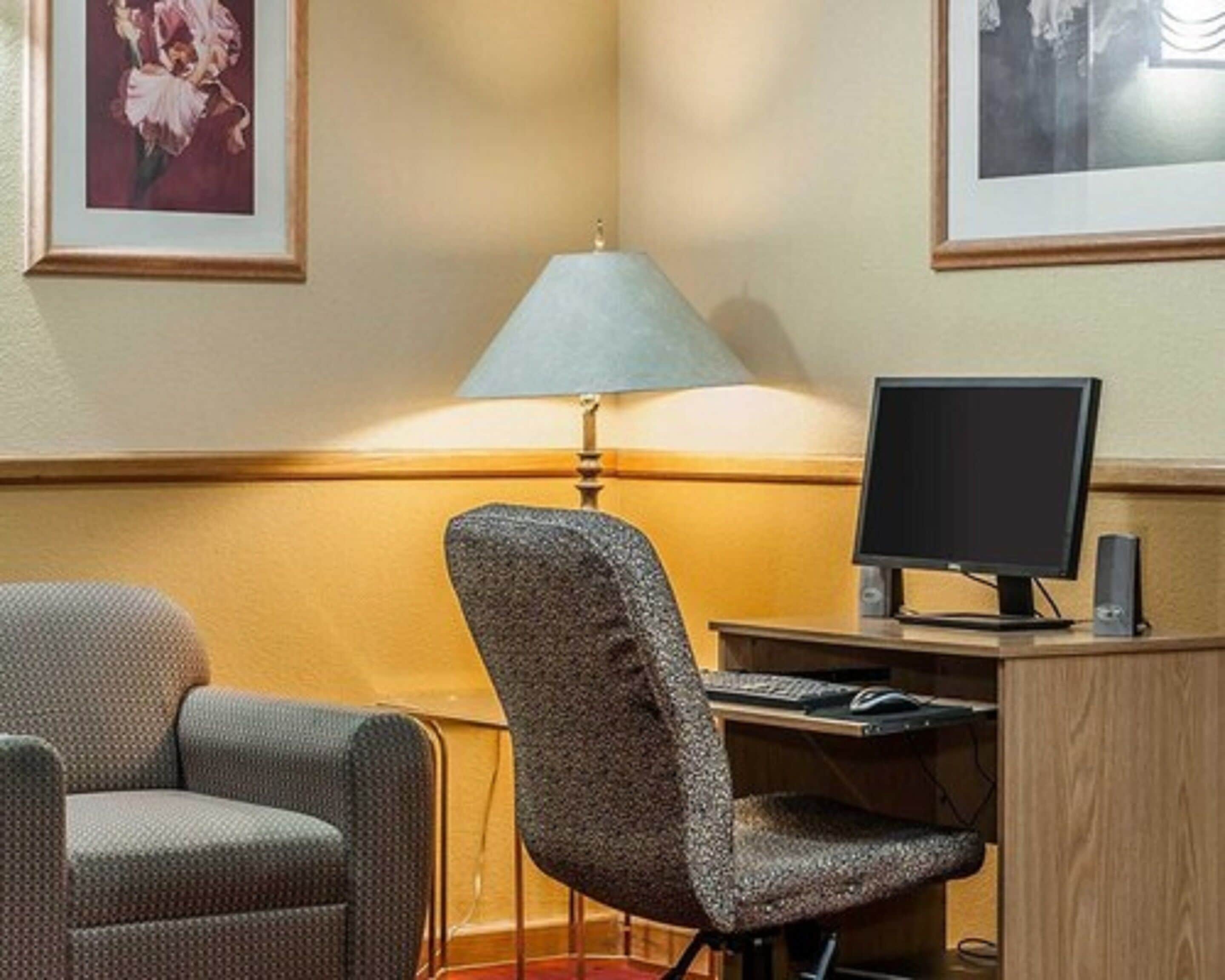 Ett hotellrum med ett skrivbord, en dator, en lampa och två stolar.