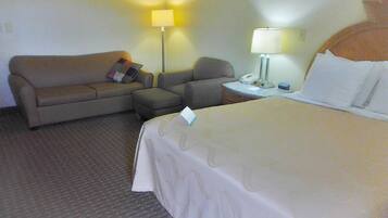 Una habitación de hotel con cama, sofá, sillón, mesita de noche y dos lámparas.