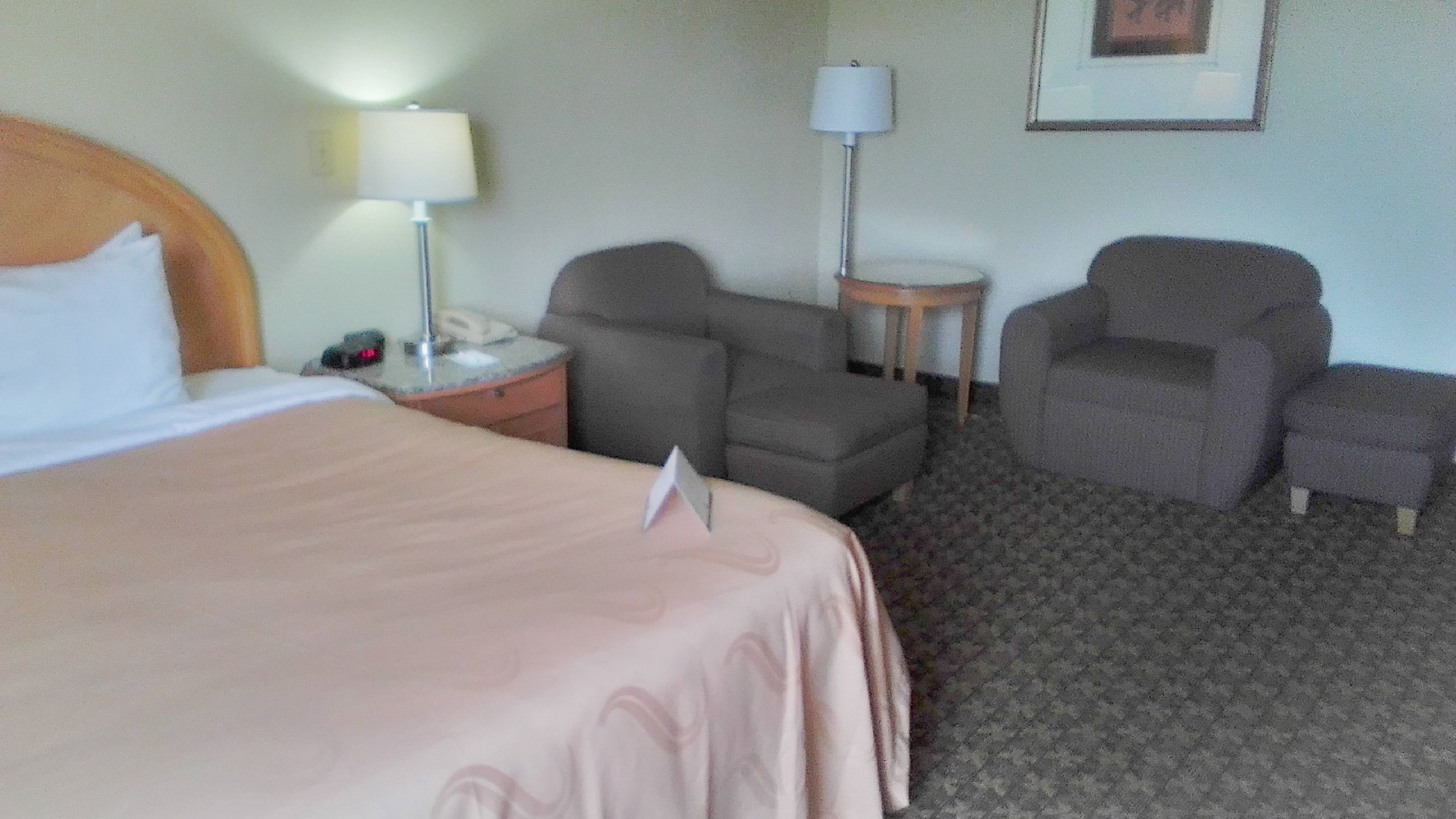 A hotel room with a bed, two armchairs, a small table with a lamp, and a framed picture on the wall.