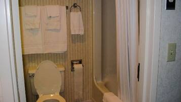 Un baño con inodoro, toallero con dos toallas, cortina de ducha y dispensador de papel higiénico.