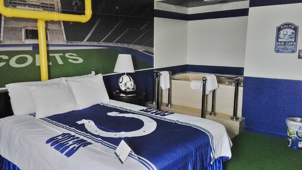 Une chambre d’hôtel avec un lit orné du logo des Colts, une table de chevet avec un casque et un porte-serviettes.