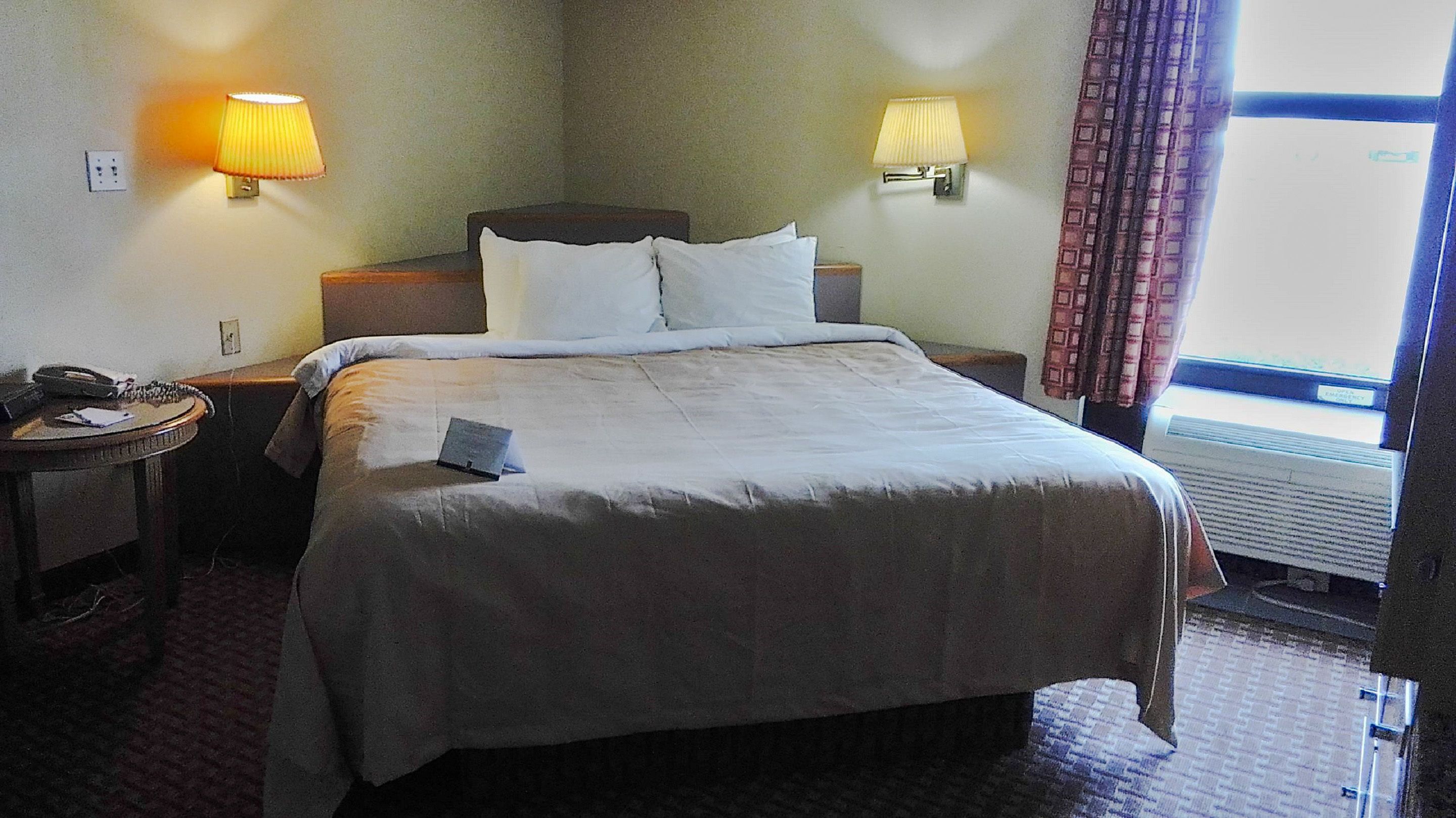 A hotel room with a large bed, two bedside lamps, a telephone, and a window with curtains.