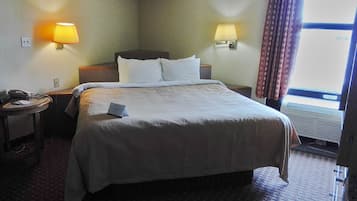 A hotel room with a large bed, two bedside lamps, a telephone, and a window with curtains.