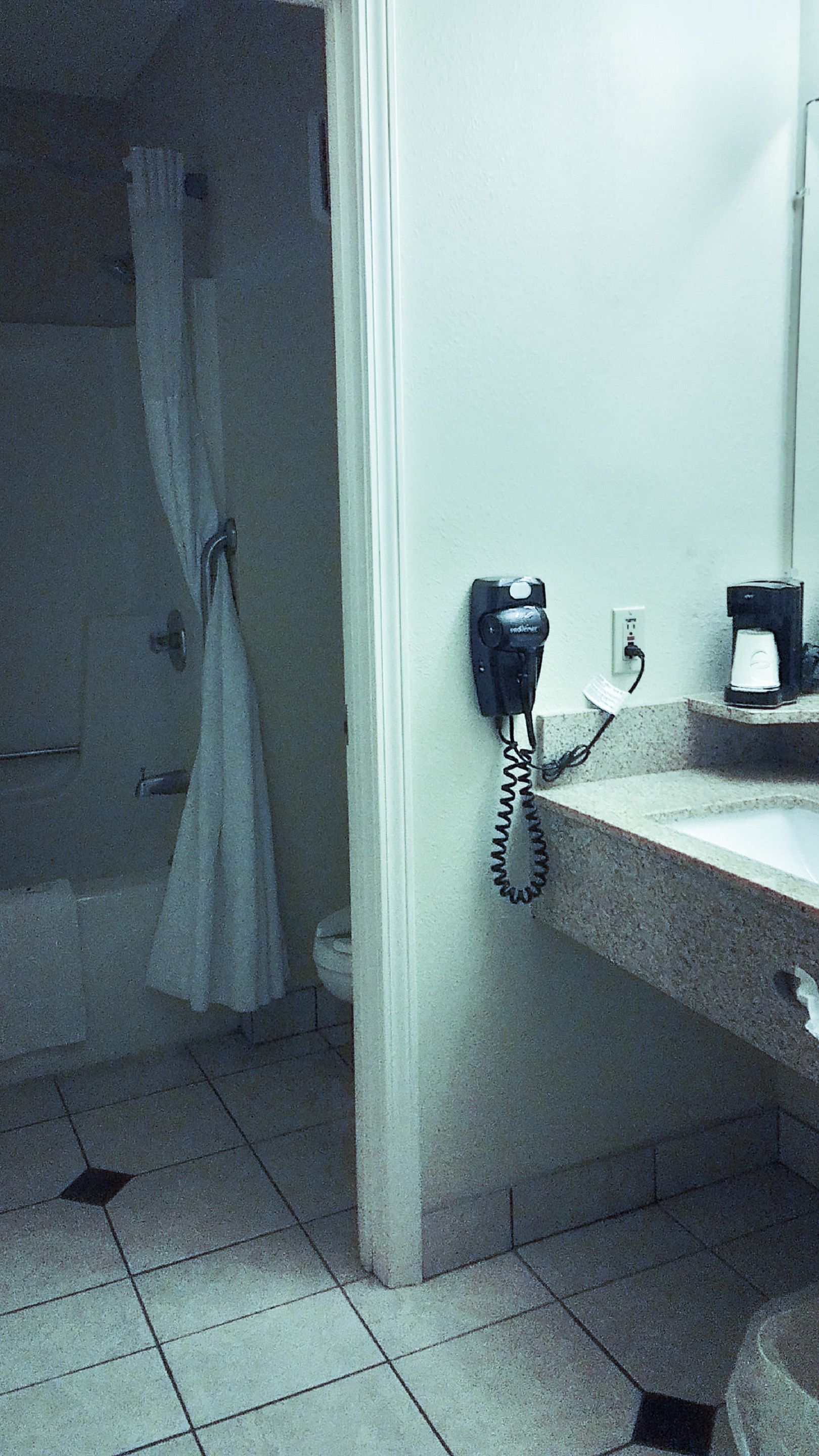 A bathroom with a telephone, a coffee maker, and a shower curtain.