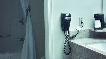 A bathroom with a telephone, a coffee maker, and a shower curtain.