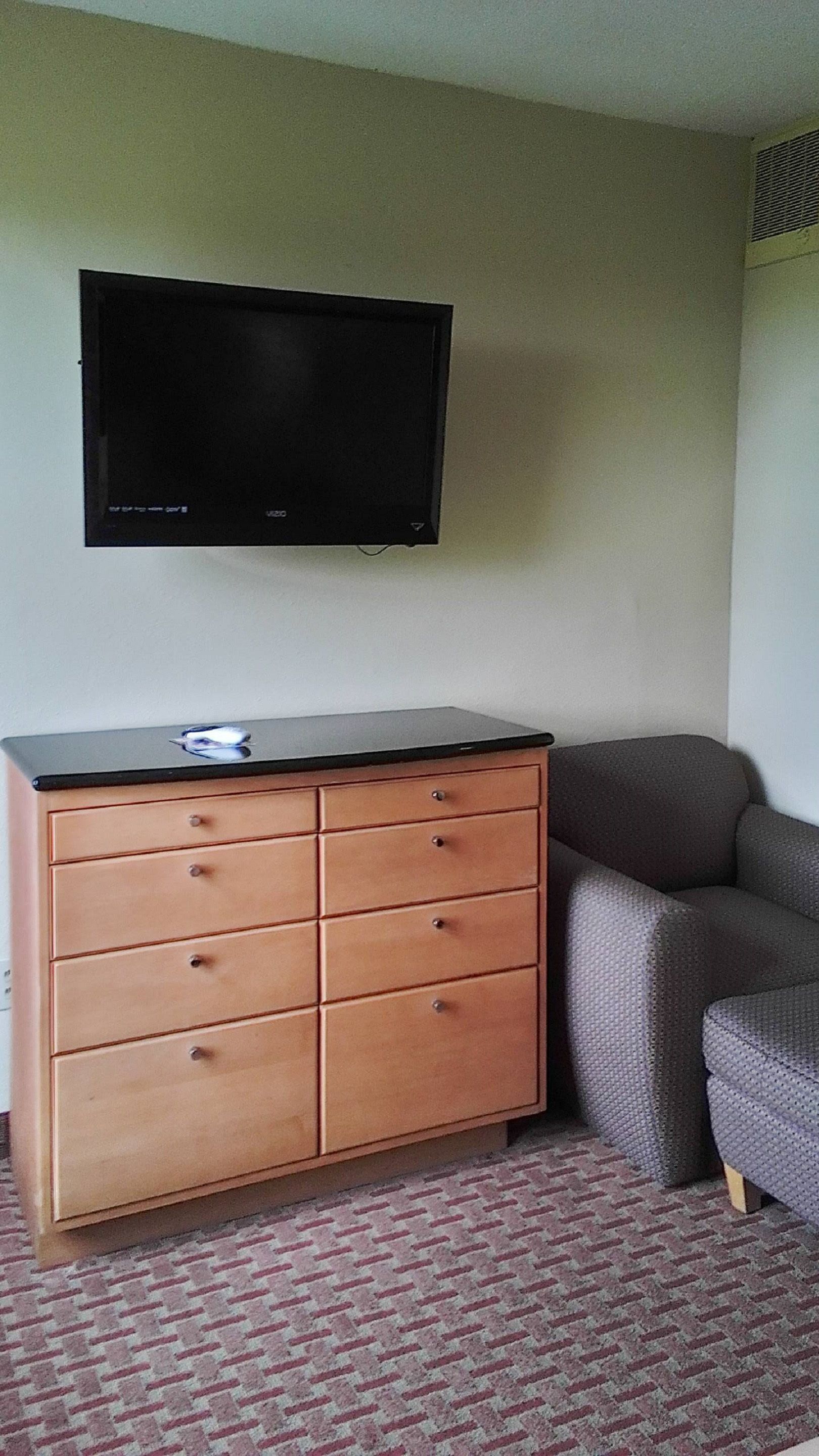 A room with a wooden dresser, a flat-screen TV mounted on the wall, and a gray sofa.
