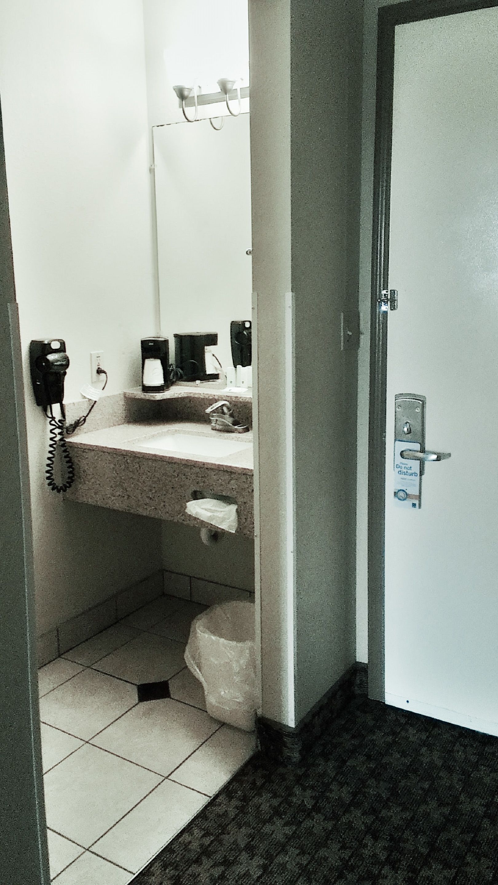 A small, narrow bathroom with a sink, mirror, and a telephone.