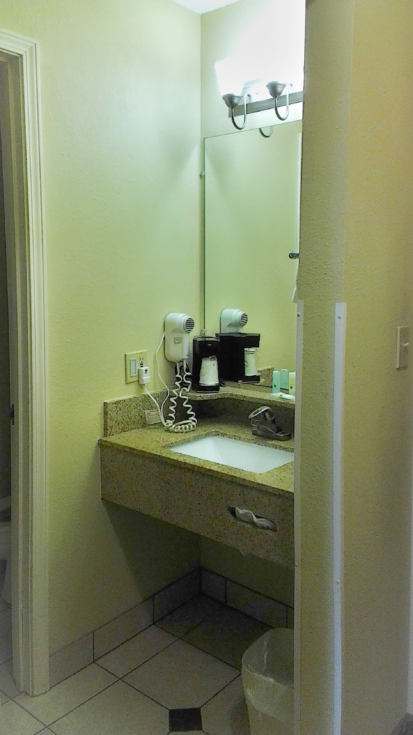 A bathroom with a sink, a mirror, a hairdryer, and a coffee maker.