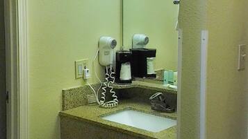A bathroom with a sink, a mirror, a hairdryer, and a coffee maker.