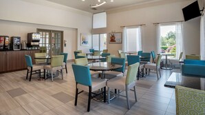 A modern hotel lobby with round tables and chairs, a kitchen area, and large windows offering views of the outdoors. - Best Western Carlton Suites (Birmingham)