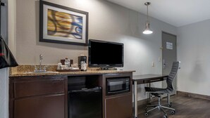 A compact kitchenette with a refrigerator, microwave, and coffee maker, a flat-screen TV, and a foldable desk with a chair. - Best Western Carlton Suites (Birmingham)
