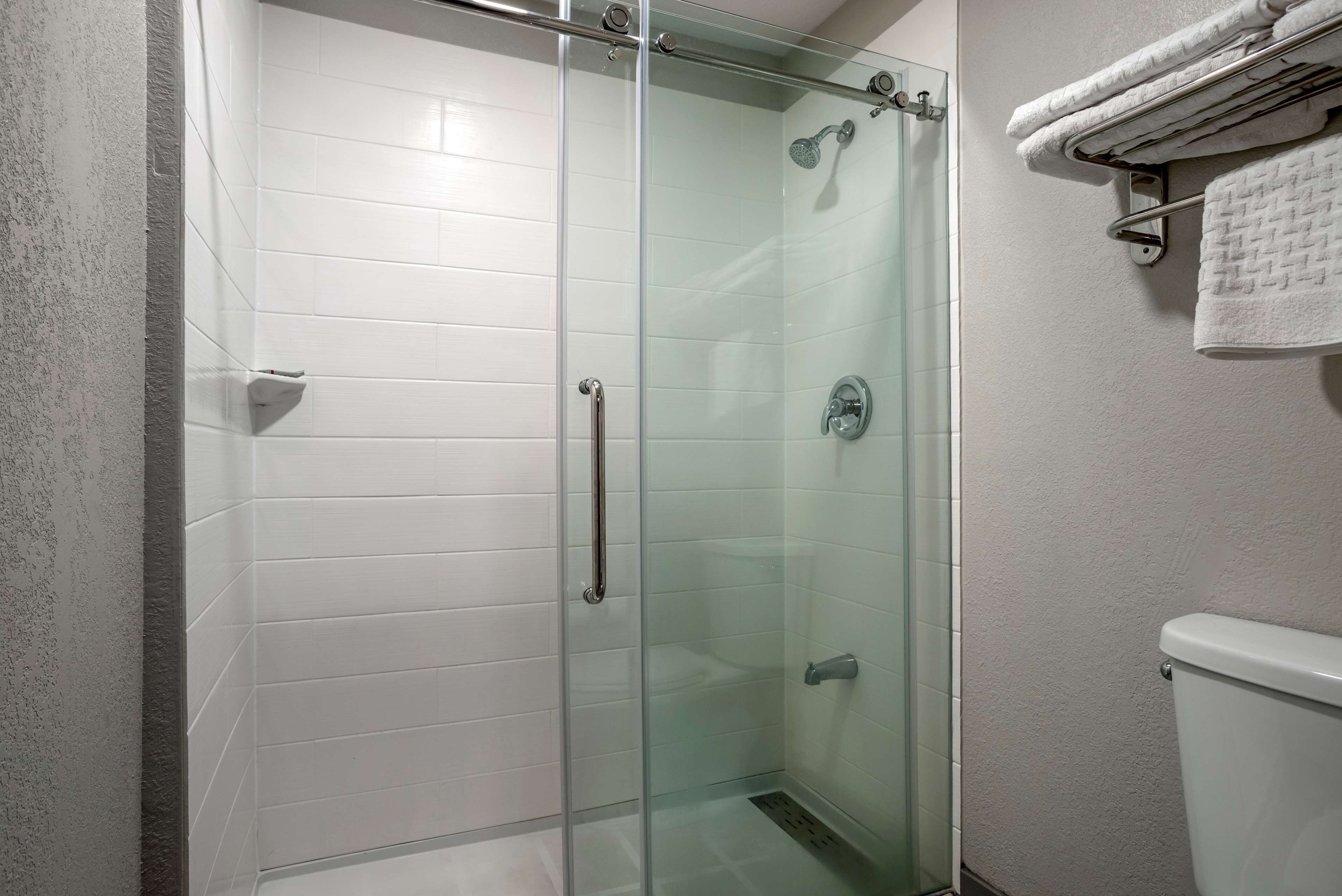 Un baño moderno con cabina de ducha de vidrio, paredes con azulejos blancos y un inodoro a la vista.