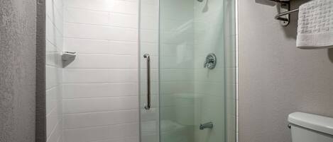 Un baño moderno con cabina de ducha de vidrio, paredes con azulejos blancos y un inodoro a la vista.
