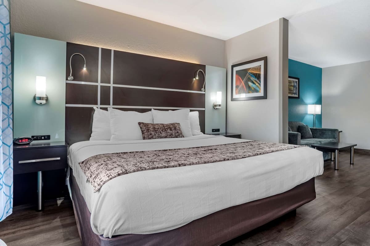 A hotel room with a large bed, bedside tables, a desk, a chair, and a wall-mounted lamp.