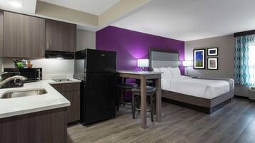A modern hotel room with a kitchen area, a dining table, and a bed.