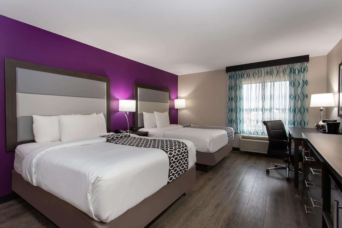 A hotel room with two beds, a desk, a chair, and a window with curtains.