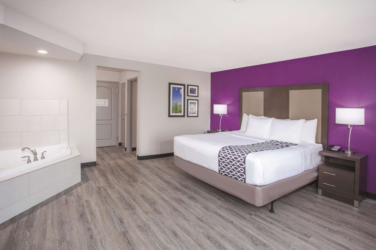 A hotel room with a large bed, a separate bathroom with a bathtub, and a wooden floor.
