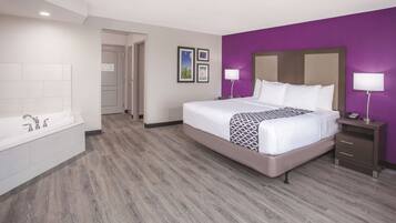 A hotel room with a large bed, a separate bathroom with a bathtub, and a wooden floor.