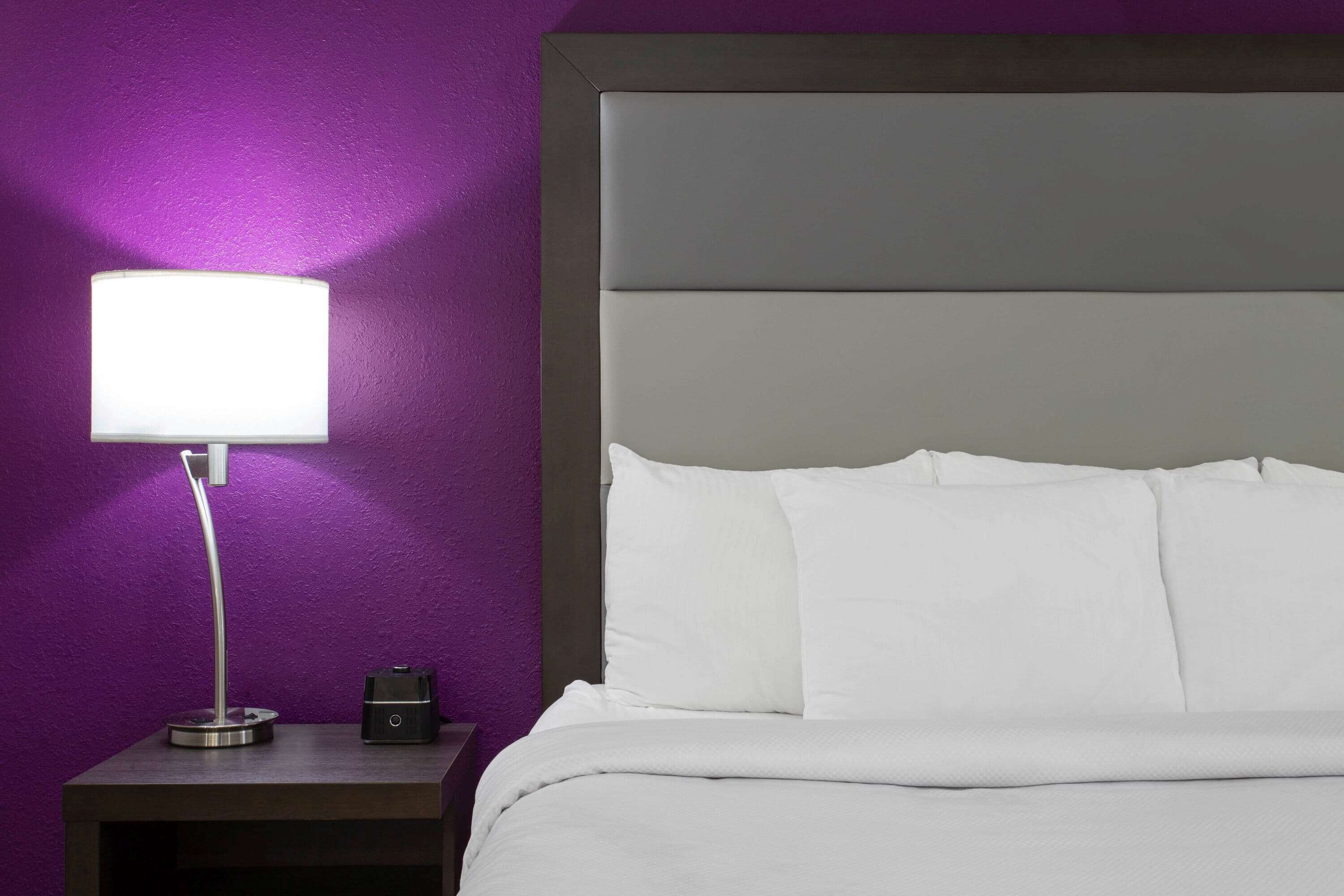 Ein ordentlich bezogenes Bett mit weißen Leinen und einem modernen Nachttisch mit Lampe.