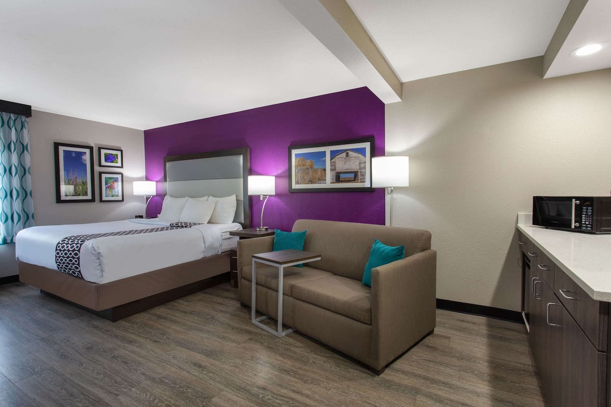 A hotel room with a bed, a sofa, a small table, a microwave, and a cabinet.