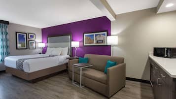 A hotel room with a bed, a sofa, a small table, a microwave, and a cabinet.